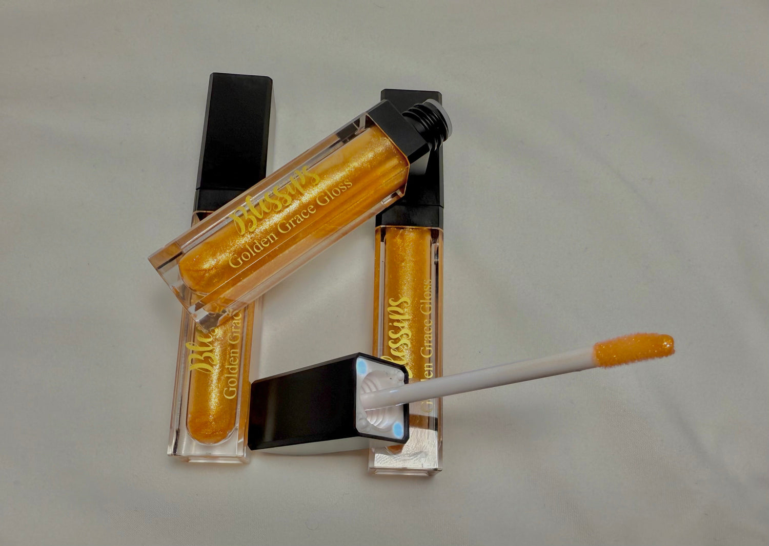  Our Golden Grace LED Lip Gloss is a smooth, moisturizing gold shine with a built-in LED light for precise application. It features a sleek tube with the Blessips logo and a mirror.